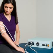 Woman sitting with PEMF-120 Machine and treatment cable wrapped around arm