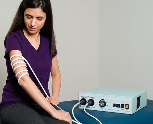 Woman sitting with PEMF-120 Machine and treatment cable wrapped around arm